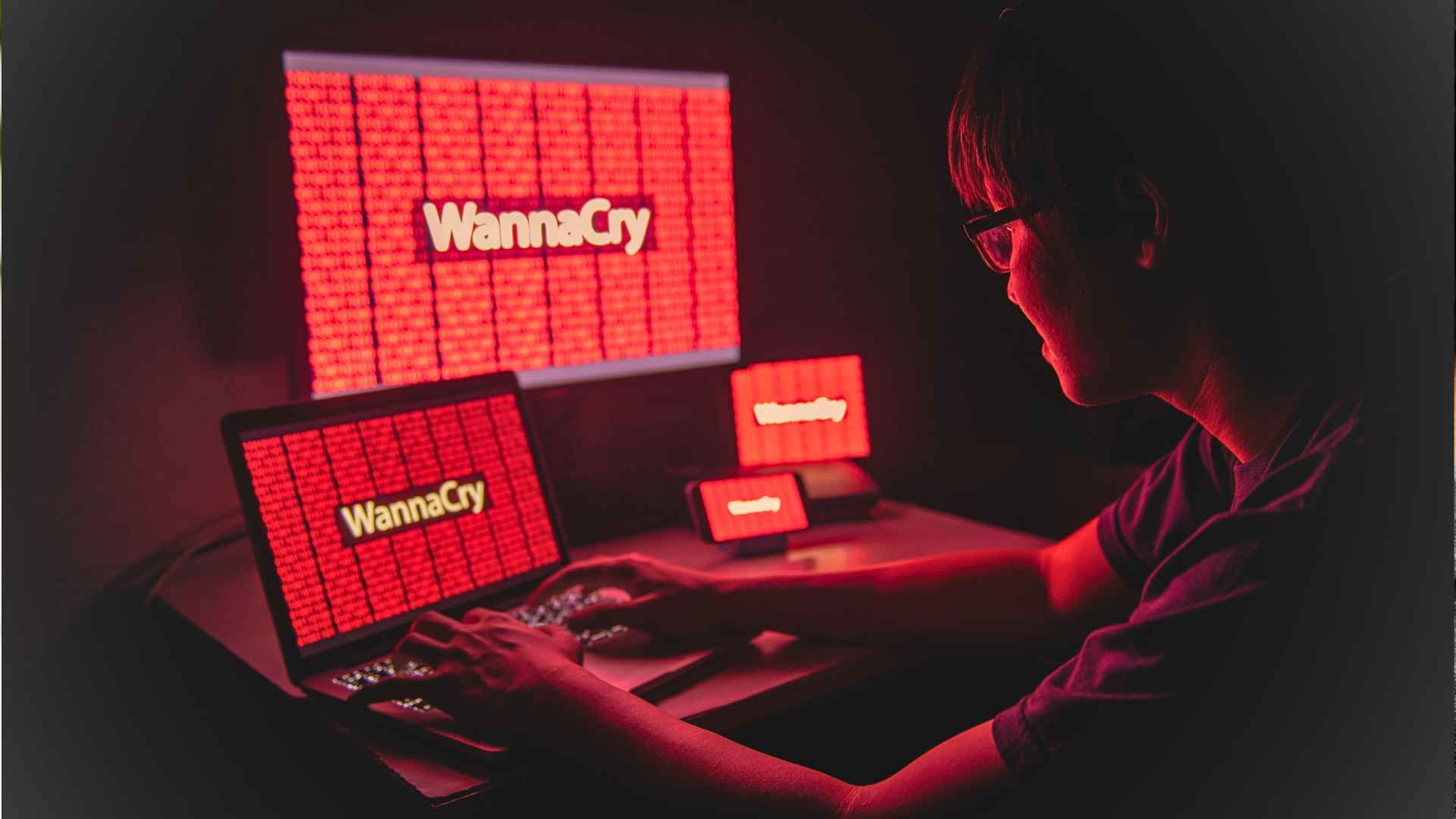 person sitting at desk with laptop computer monitor phone and tablets all with the wannacry ransomware warning on screen