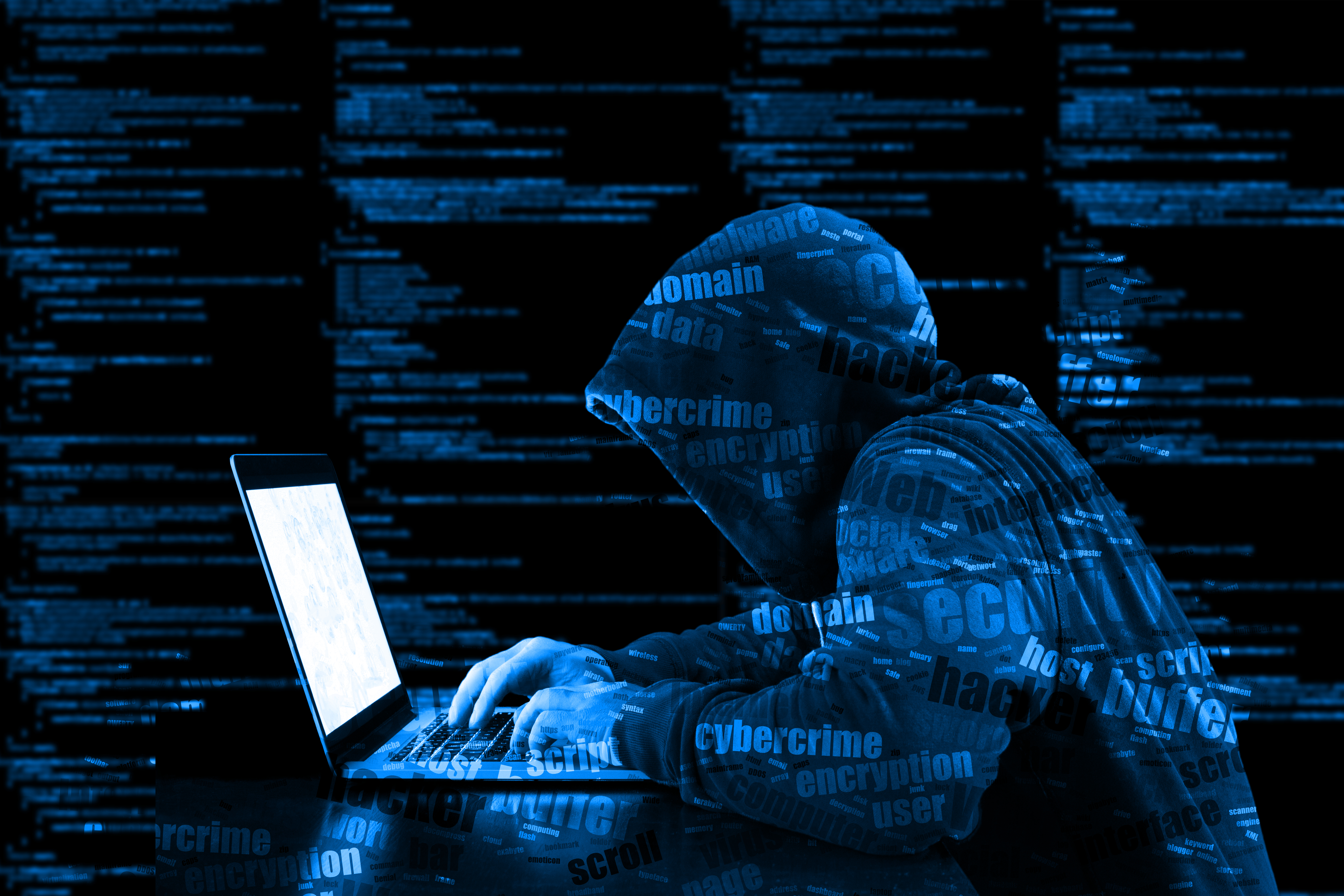 cyberattack criminal leaning over typing on laptop keyboard with cybersecurity text overlayed