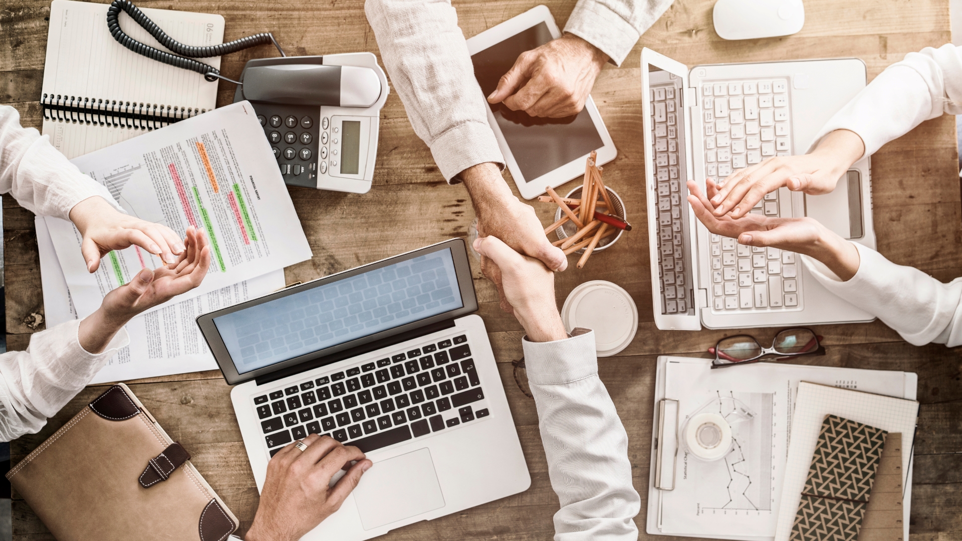 managed it support shaking hands across a desk with IT devices on table