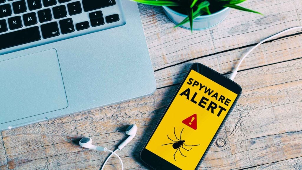 phone with spyware alert symbol on it next to a laptop keyboard