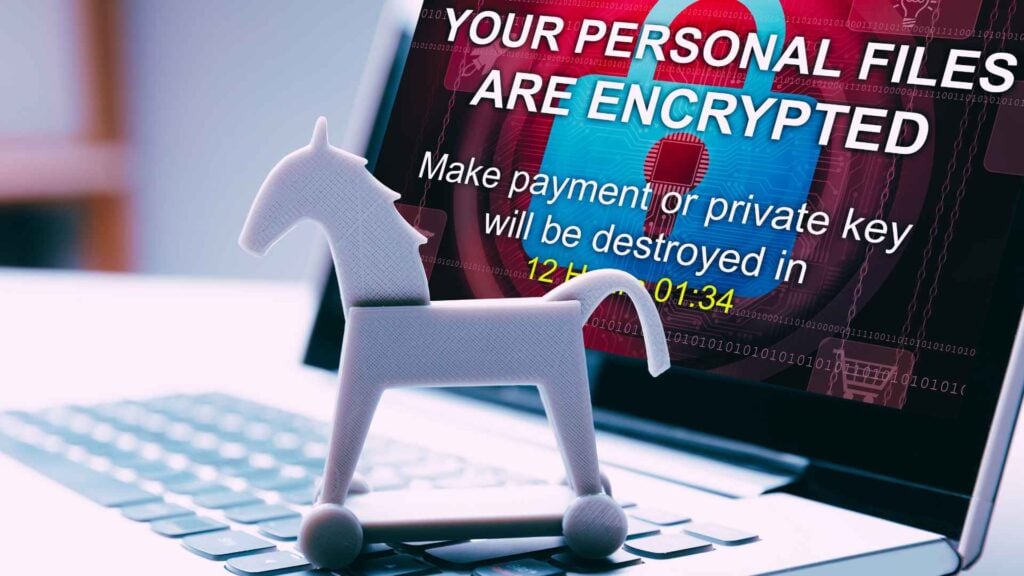 trojan horse toy sitting on top of laptop keyoard with malware warning on screen about personal files being encrypted and to pay ransom