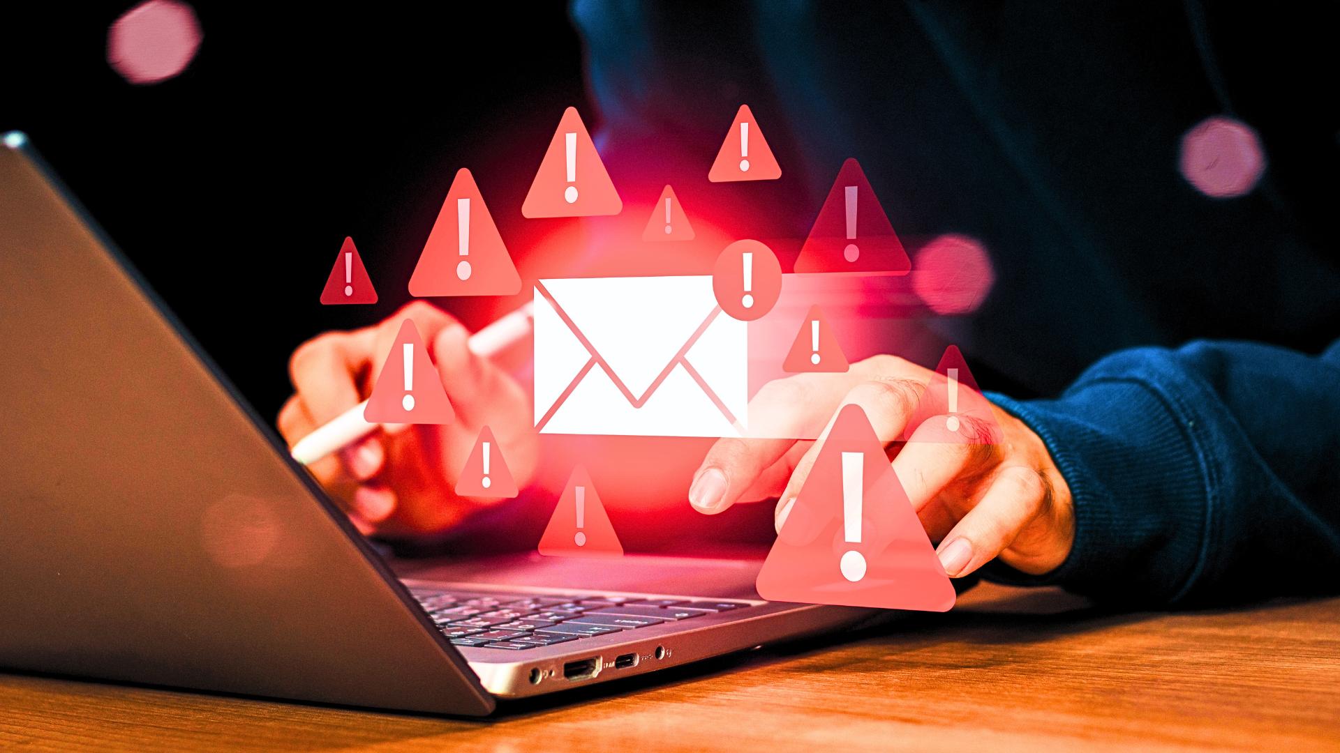 person typing on laptop keyboard with email security warning symbols
