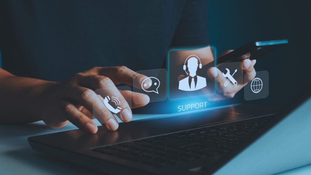 business person holding phone with an it support services logo hovering over laptop keyboard