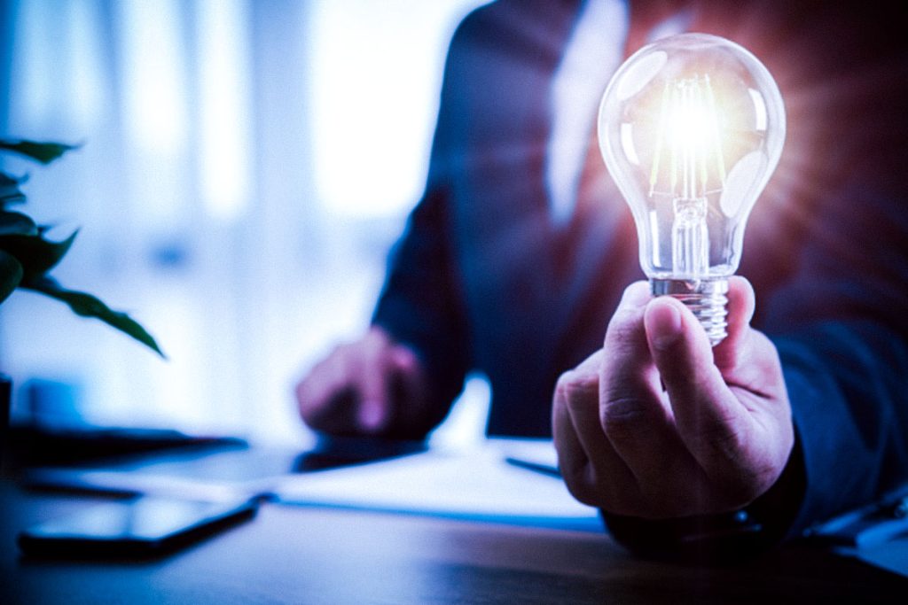 business person holding a lightbulb lit up sitting at their desk