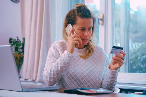 woman on phone looking confused and looking at credit card due to a scam