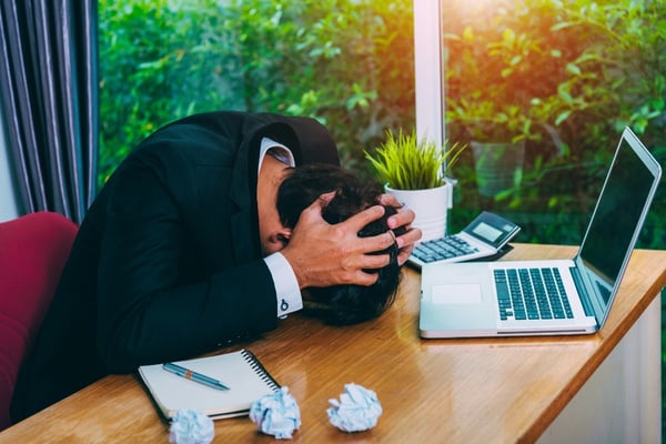 business man sitting at desk frustrated due to IT downtime with laptop in front of him