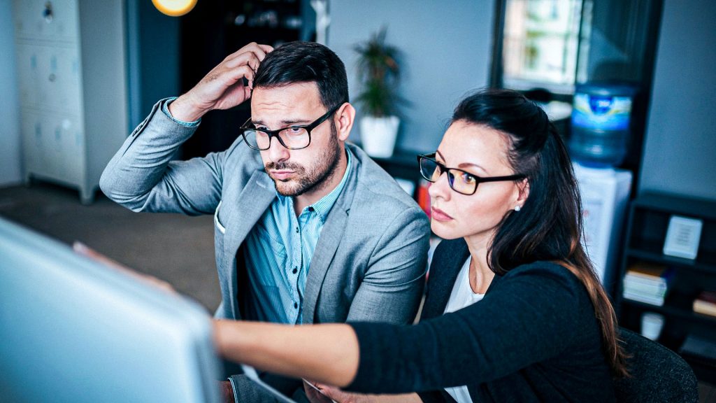 Business man looking confused as a business woman explains how to do DIY IT on a computer