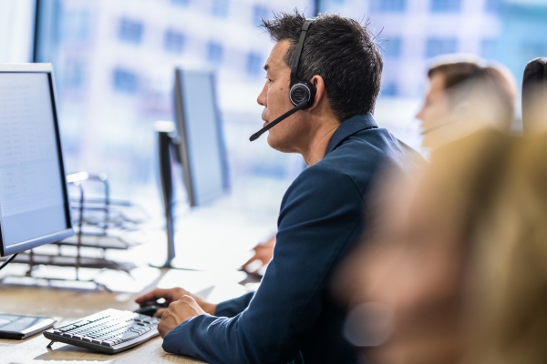 IT support worker wearing headphones talking to customer whilst typing on computer