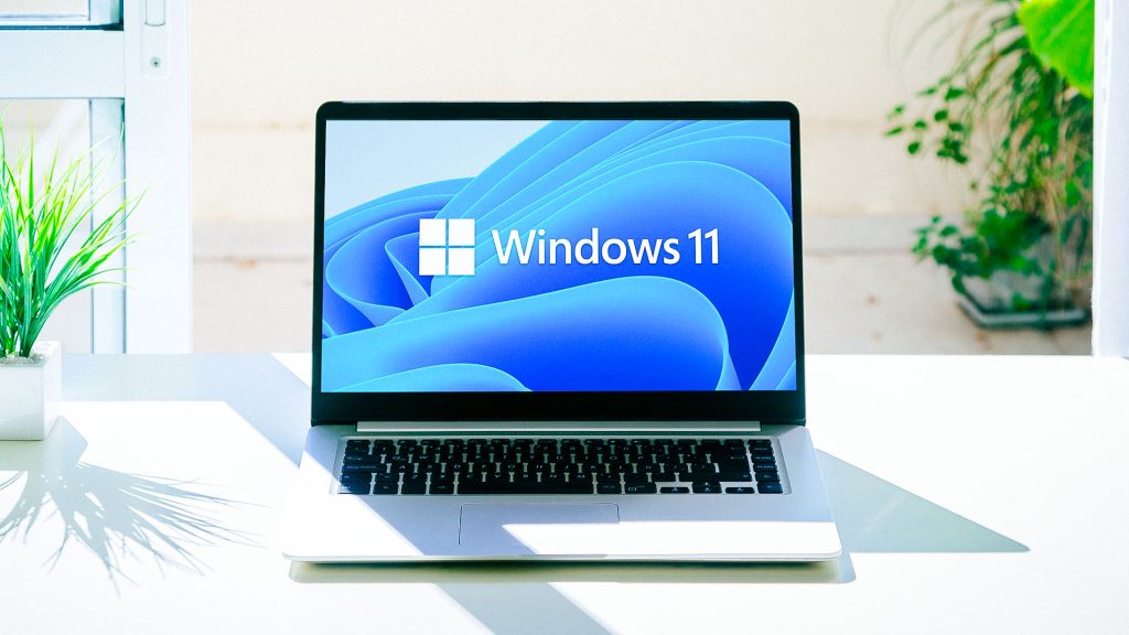 laptop sitting on a work office desk with the windows 11 logo on screen