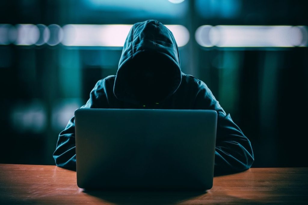 hacker sitting at desk typing on a laptop performing advanced persistent threat cyberattack